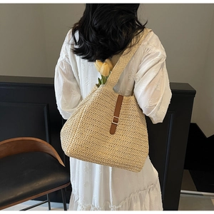 Detail of beige woven straw shoulder bag featuring brown leather strap and silver buckle