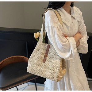 Détail d'un sac cabas en paille avec bandoulière en cuir brun et boucle sur robe blanche