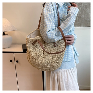 Detail of woven straw tote bag with brown leather strap worn by a woman in a casual setting