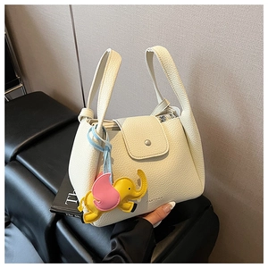 Detail of white lychee leather bucket bag with top handle and elephant charm decoration