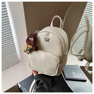 Détail d'un mini sac à dos blanc cassé en similicuir avec charm ours et fermeture éclair