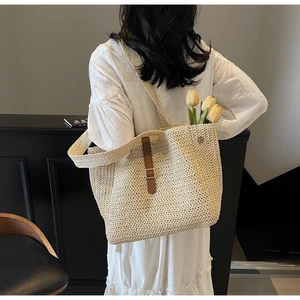 Close-up of beige woven tote bag with brown leather strap and buckle detail