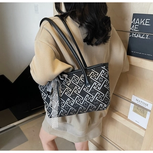 Detail of a black patterned tote bag with white lace ribbon and leather shoulder strap