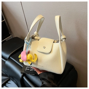 Detail of creamy white pebbled leather handbag with elephant charm and debossed logo