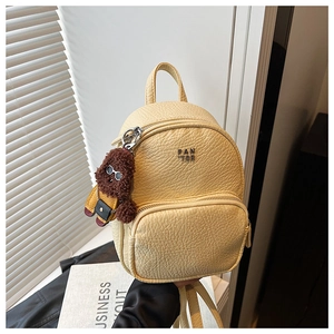 Détail d'un mini sac à dos en cuir litchi jaune avec logo métal et charme en peluche