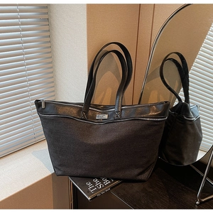 Close-up of black denim tote bag with leather straps and decorative metal plaque detail