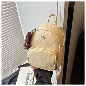Détail du mini sac à dos jaune avec texture grainée et breloque ours en peluche