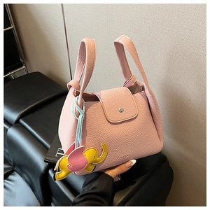 Detail of pink pebbled leather bucket bag with a yellow elephant charm on a sofa