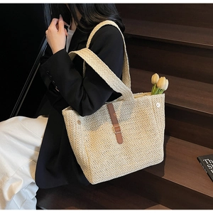 Detail of woven straw tote bag with brown leather buckle and wide knit shoulder strap