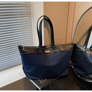 Detail of blue denim tote bag with black leather handles and silver metal hardware