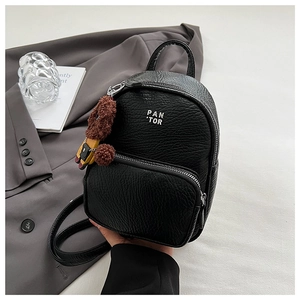 Gros plan d'un mini sac à dos noir avec logo argenté et breloque ours en peluche marron