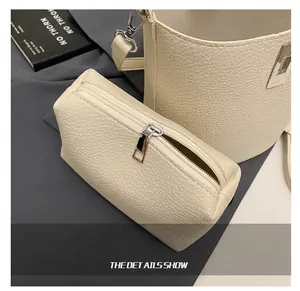 Detail shot of a cream-colored pebbled leather pouch with a silver metal zipper and hardware
