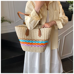 Straw tote bag with colorful woven stripes on a model in a yellow shirt and white skirt
