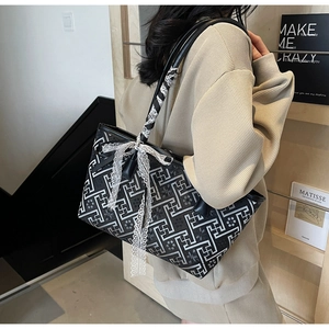 Detail of black tote bag with white geometric pattern, silk scarf and lace bow charm