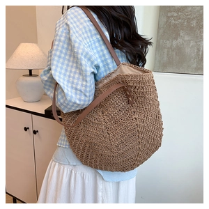 Detail of hand-woven straw tote bag featuring premium brown leather shoulder straps