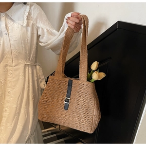 Detailed close-up of a woven straw tote bag with black strap and silver buckle accent