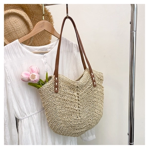 Detail of straw woven tote bag featuring brown leather straps with white cross stitching
