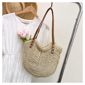 Detailed view of braided straw tote bag with sturdy brown straps and white stitching