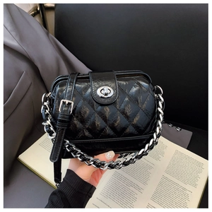 Detail of black quilted chain bag with silver turn-lock clasp on a lifestyle book background