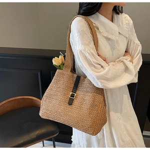 Detail of beige woven tote bag with black leather strap and golden buckle on model