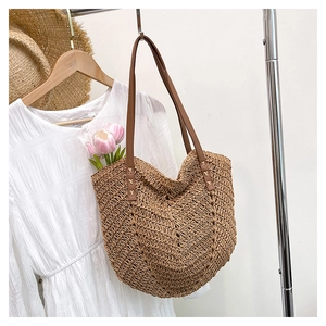 Detail of handwoven straw tote bag with brown leather straps hanging by white dress