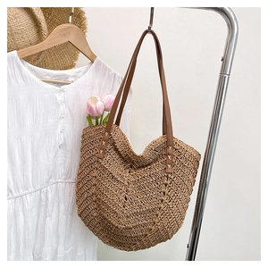 Close-up of woven straw tote bag with brown leather handles and flower detail