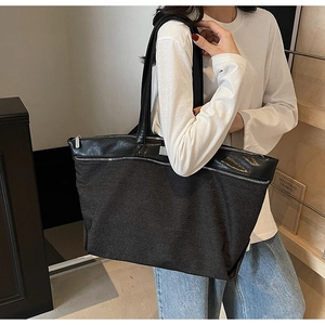 Detail of a black large capacity tote bag with leather trim on a model's shoulder