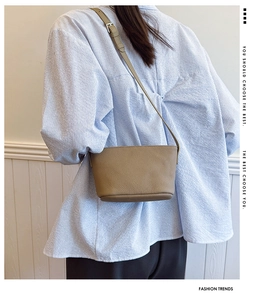 Model wearing a minimalist khaki leather bucket bag with an adjustable shoulder strap