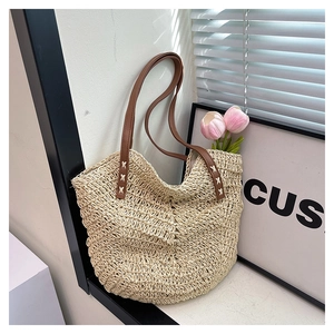 Detailed view of handmade woven straw tote texture with brown leather shoulder straps