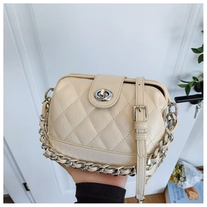 Close-up of cream quilted crossbody bag featuring silver turn-lock and chain strap detail