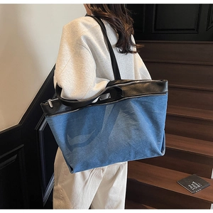 Detail view of a large denim and black leather tote bag worn as a shoulder bag