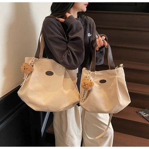 Détail de sacs cabas en toile blanc cassé avec anses en cuir marron et pendentif ours