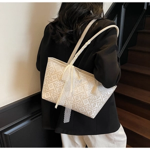 Fashionable beige tote bag with geometric patterns and lace bow detail on a model