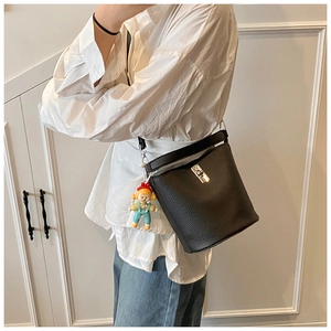 Close-up of black leather bucket bag with silver lock and a cute cartoon doll charm