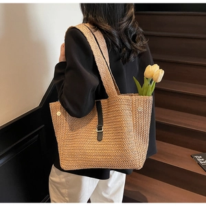 Detail of woven straw tote bag with black leather buckle and handle in lifestyle setting