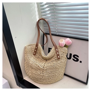 Detail of beige straw tote bag featuring brown leather handles and decorative white cross-stitching