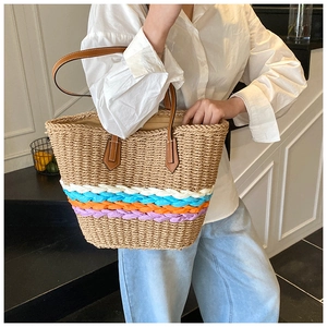 Detail of hand-woven straw tote bag with multi-color stripes and brown leather handles