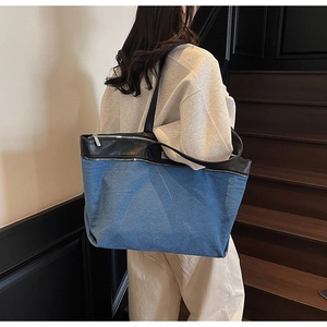 Detail of denim and black leather tote bag featuring large silver metal zipper accents