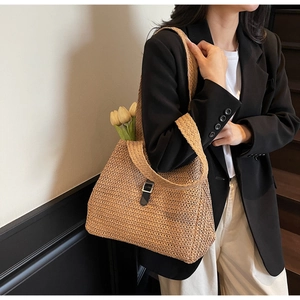 Detail of woven straw tote bag with black leather strap and silver metal buckle accent