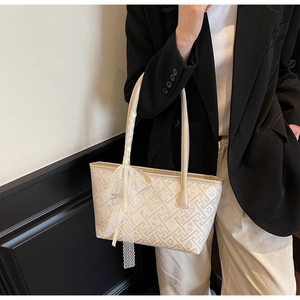 Detail of cream tote bag with geometric jacquard pattern and white lace bow accessory