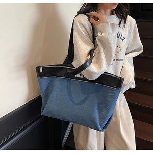 Detail of blue denim tote bag with black leather straps and silver zipper closure