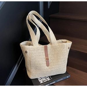 Detailed texture of beige woven tote bag featuring brown leather strap and golden buckle