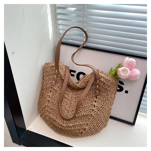 Detail of woven straw tote bag featuring wavy texture and brown faux leather handle