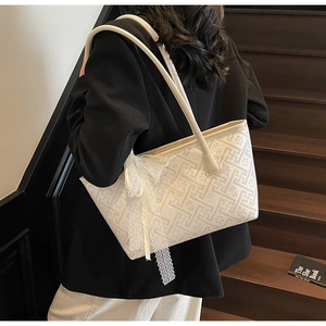Detailed shoulder view of a beige jacquard tote bag with lace bow on indoor stairs