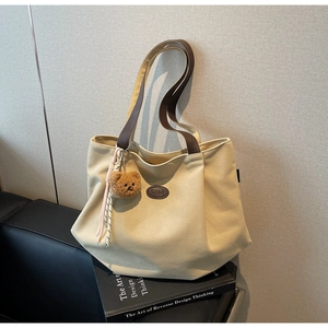 Détail du sac fourre-tout en toile avec anses brunes, logo cuir et breloque ours