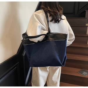Detail of blue denim tote bag featuring black leather trim and silver zipper accents
