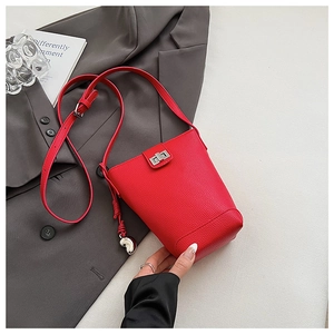 Detail of red lychee grain leather bucket bag featuring a silver twist lock and heart charm