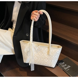 Detail of cream tote bag featuring geometric embroidery and lace bow on the handle