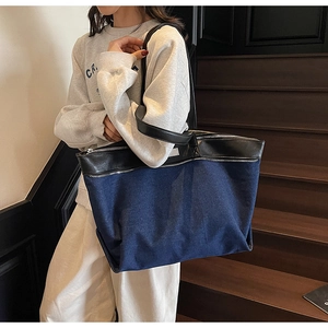 On-shoulder view of large denim and leather patchwork tote bag with silver zipper