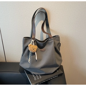 Détail d'un sac fourre-tout en toile gris foncé avec poignées en cuir et breloque ours